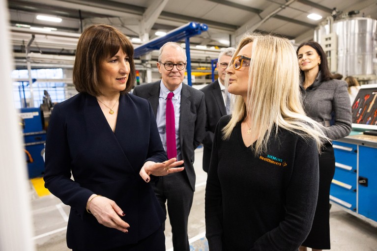 Rachel Reeves and Patrick Vallance stand on a factory floor talkng to a female employee