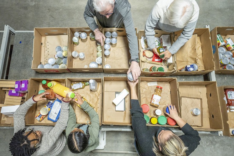 Overhead view of a groups of volunteers of various ages sorting non-perishable food items into boxes at a food bank.