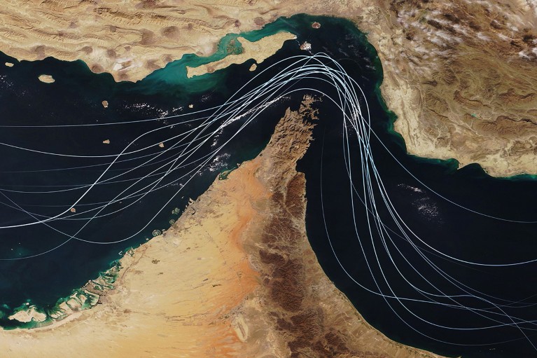 Satellite view of the Strait of Hormuz with white graphic lines representing global shipping lanes.