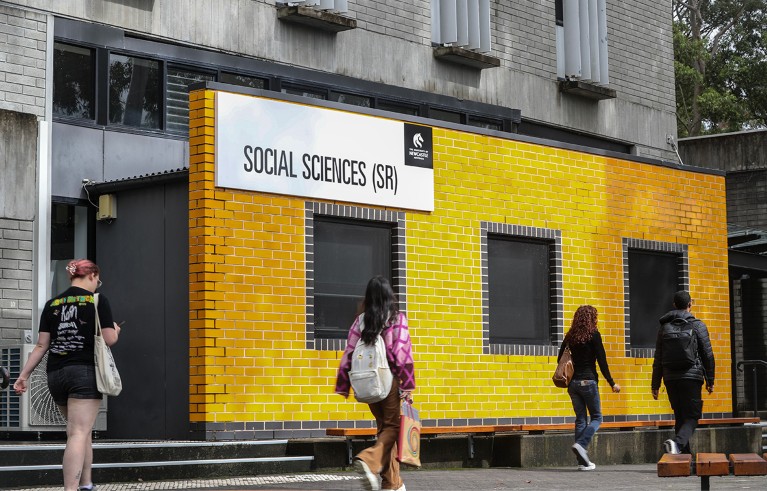 Four people walk at the University of Newcastle's Callaghan campus passing in front of the yellow wall of the social science department in Newcastle, Australia.