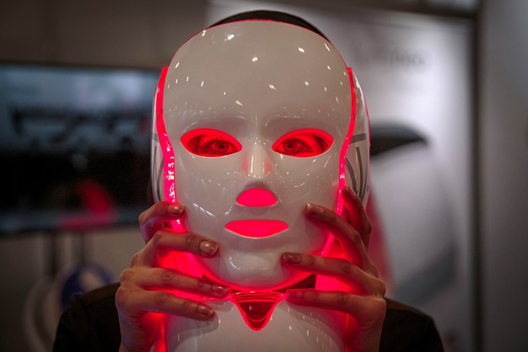 Close-up of a white, shiny face mask, emitting red light onto the face in front of which it is being held..