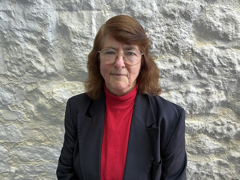 A portrait of Sue Sundstrom wearing a black blazer and red polo neck