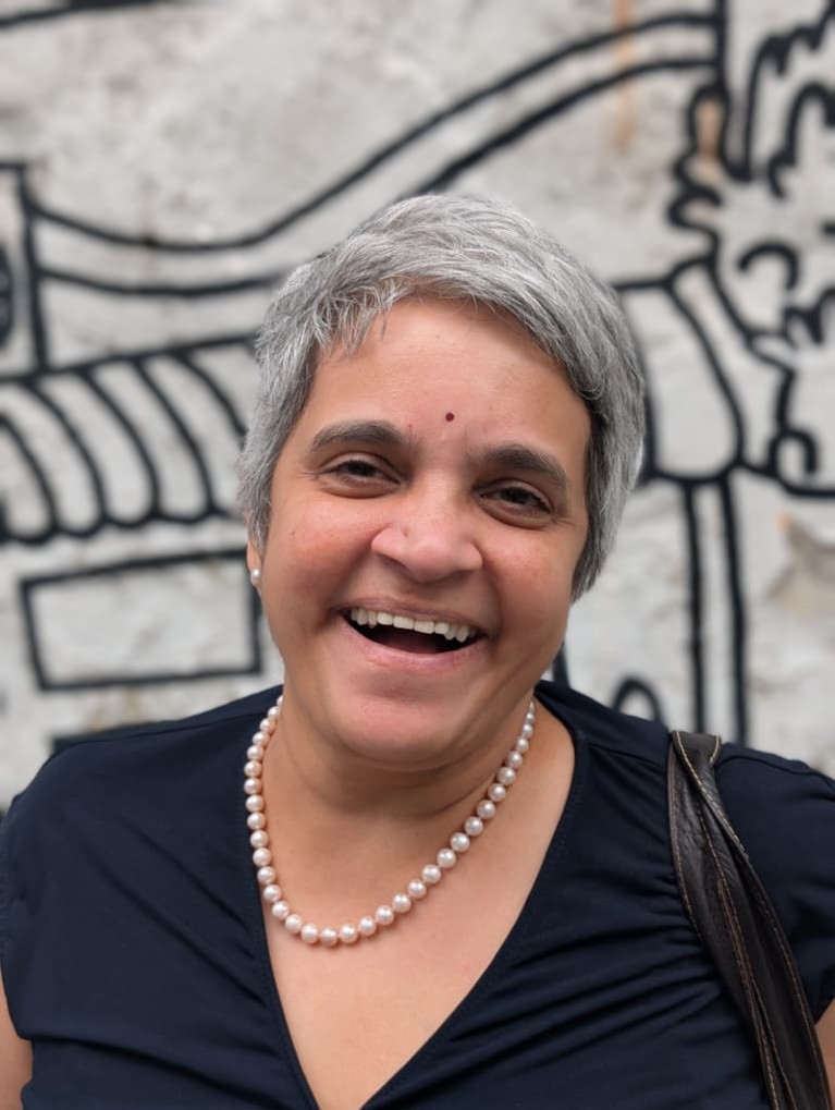 Vani Mahadevan smiles as she stands in front of a black and white line art mural