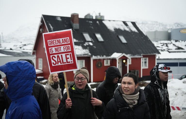 Young people with a red placard protest against US President Trump. Typical Greenland house in the background.