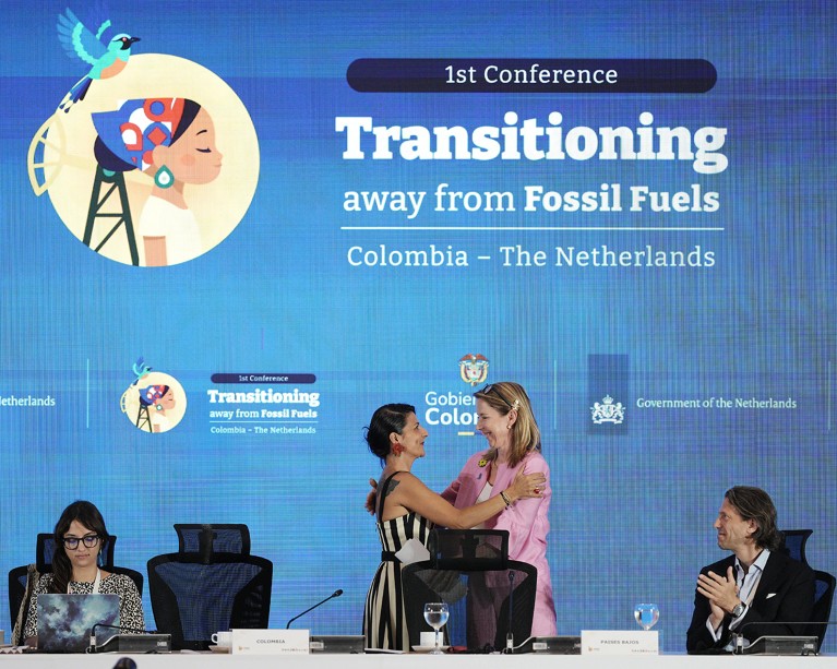 International climate ministers embrace at the head table during a conference.