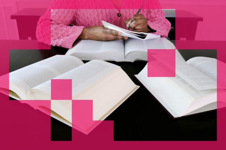 View of lady in pink jumper taking notes from three open books on a table.