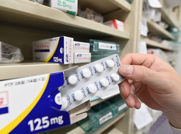 A close-up view of a hand removing a blister pack of Xocova tablets from their pack in a pharmacy in Japan.