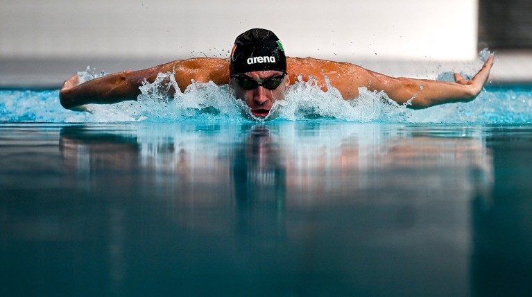 A competitive swimmer rises above the pool surface mid-stroke.