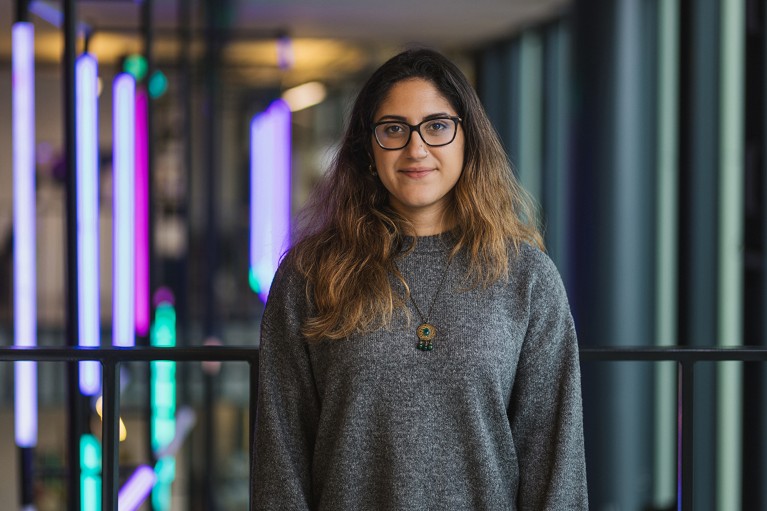 Head and shoulders portrait of Layla Hosseini-Gerami facing forwards. Behind her to the left are bright coloured vertical lights.