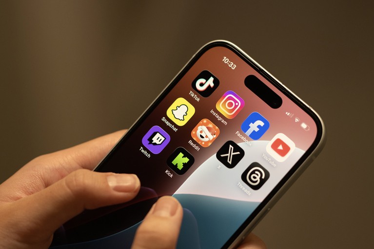 Close-up of hands holding a mobile phone with social and video streaming apps visible on the screen.