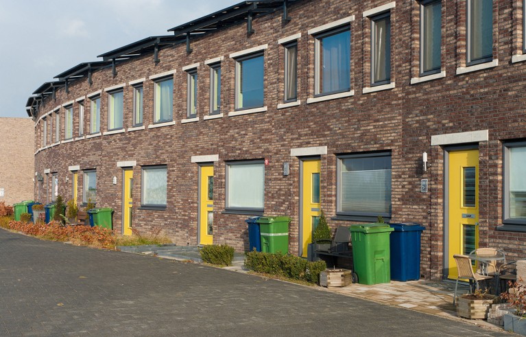 Curved row of modern brick townhouses featuring yellow front doors and large rectangular windows. Green and blue wheelie bins are placed outside each house.