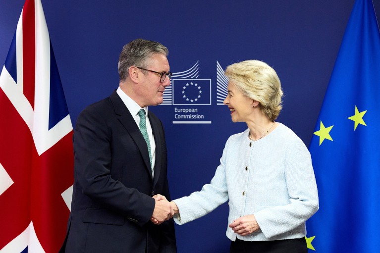 Keir Starmer shakes hands with Ursula von der Leyen in front of a European Commission logo, with a Union Jack flag on the left and The Flag of Europe on the right
