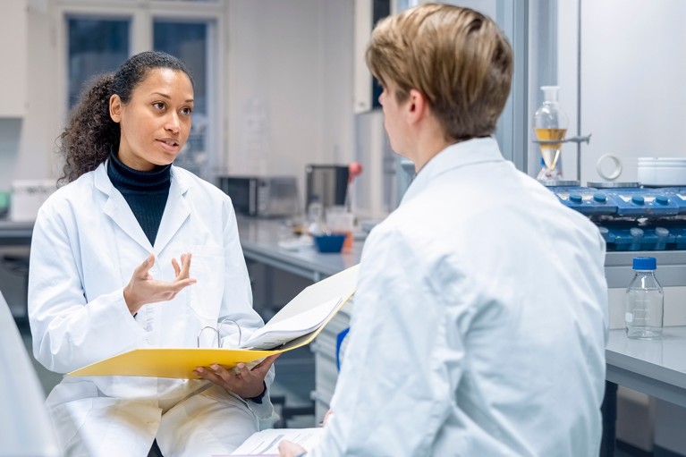 Female researcher holding a file and talking with a lab technician in a laboratory.