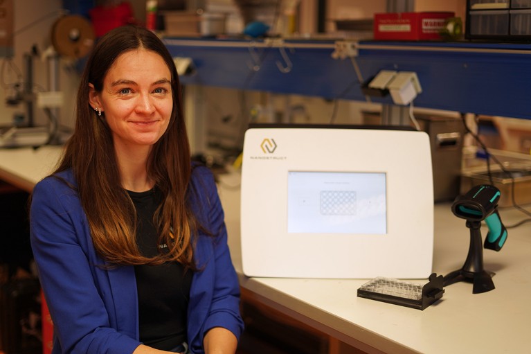 Henriette Maaß sits in her laboratory beside a NanoStruct bacterial testing machine.