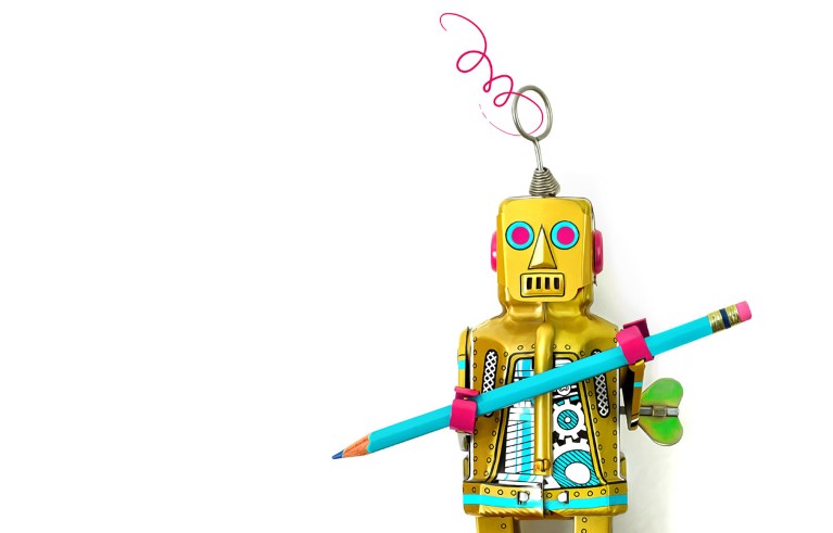 Close up of a vintage style toy robot on a white background holding a blue pencil.
