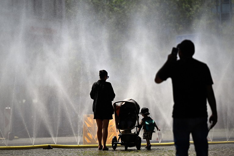 People stand near water hoses spraying mist to provide relief from summer heat, part of Cologne, Germany’s climate adaptation efforts.