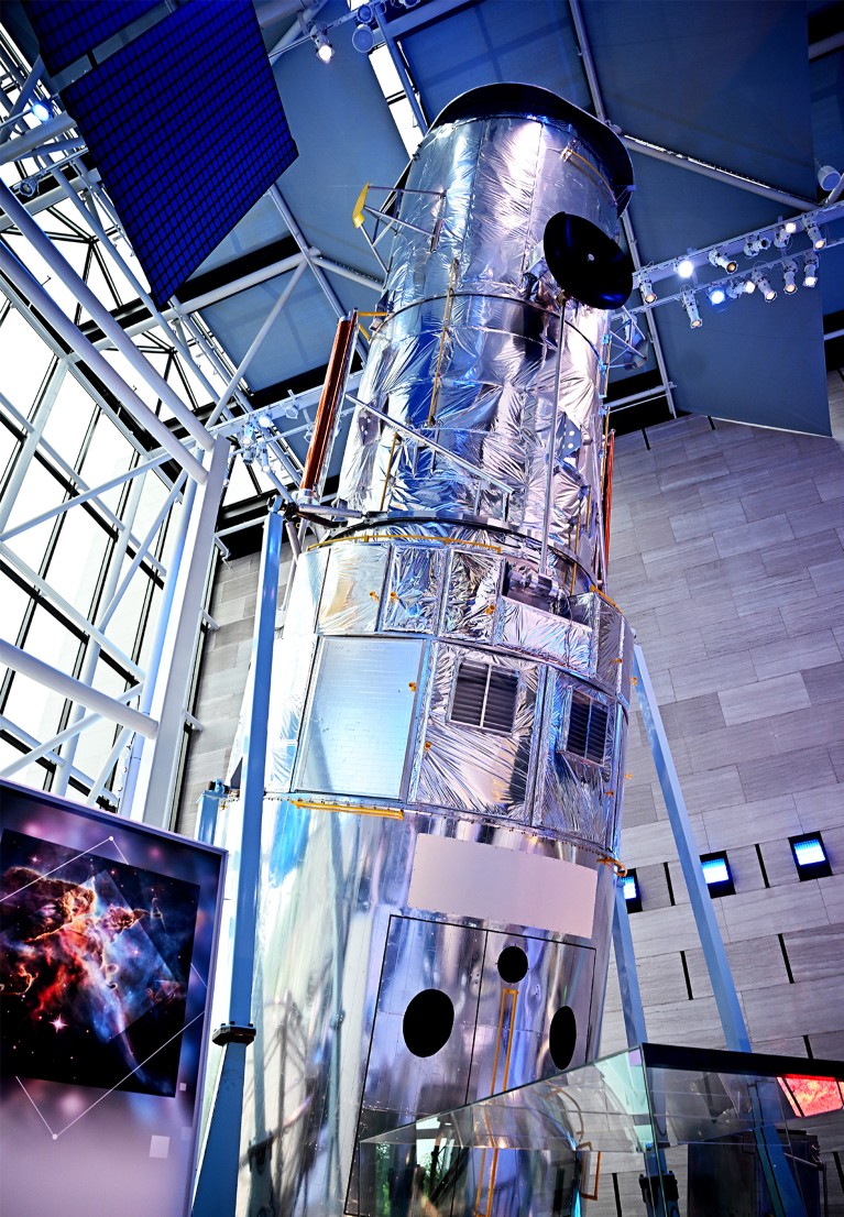 A large, cylindrical space telescope model with metallic reflective surfaces and various structural components.