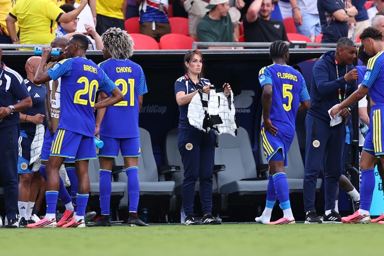 A woman holds out a white garment towards one of several men in blue football strips.