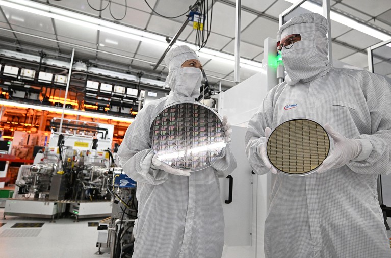 Two employees in PPE handle different-sized gallium nitride (GaN) wafers within a fully automated cleanroom at a semiconductor facility.