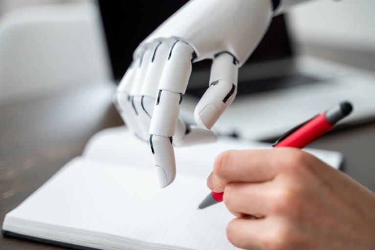 A close-up of a white robotic hand reaching towards an open notebook while a person writes with a red pen