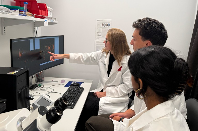 Valentina Fossati mentoring team members seated around a computer in a laboratory.