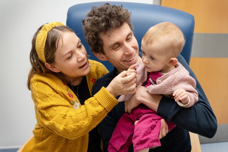 Safi Ford sits between her mother Dorka Nemeth and father Cameron Ford in a chair.