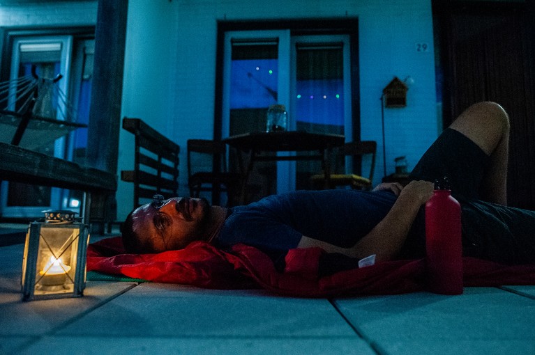 A man sleeps on a terrace at night on a mat beside a small lantern during a heatwave in the Netherlands.