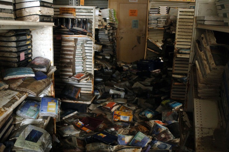 A large amount of damaged books are scattered across a floor and shelves with signs of flood damage.