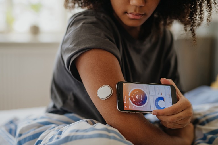 Close-up of teenage girl holding a smartphone near a glucose monitor on her upper arm.