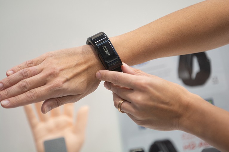Close-up view of the forearm and hand with a black blood pressure cuff on the wrist. The second hand is touching the monitor.