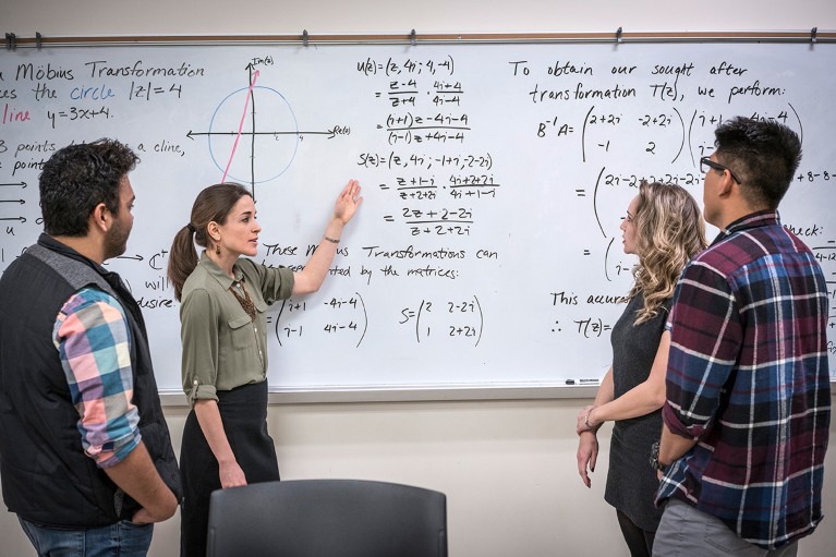 Mathematics university students discussing equations written on a whiteboard.