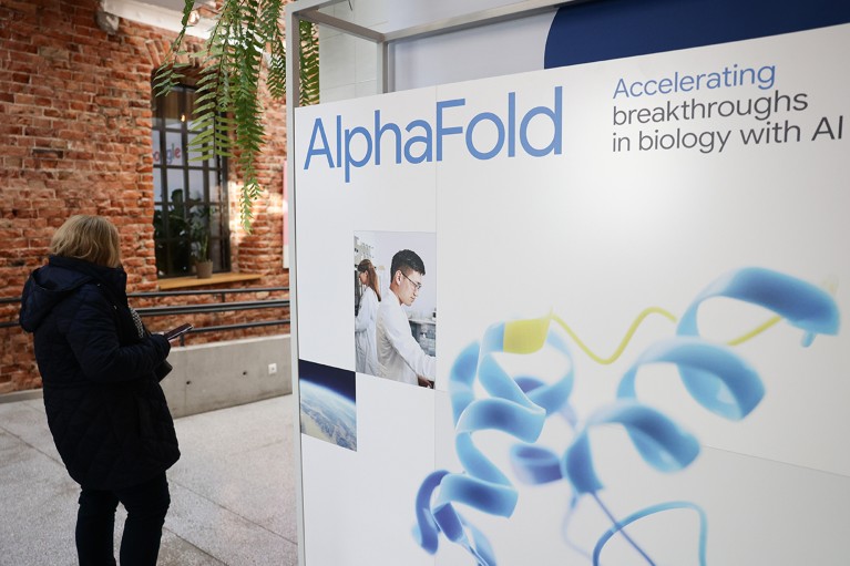 People walk past the AlphaFold logo on a conference venue display board.