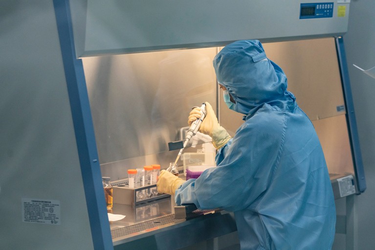 A lab technician wearing PPE, working in a fume hood in a Chinese laboratory developing CAR-T cell therapies.