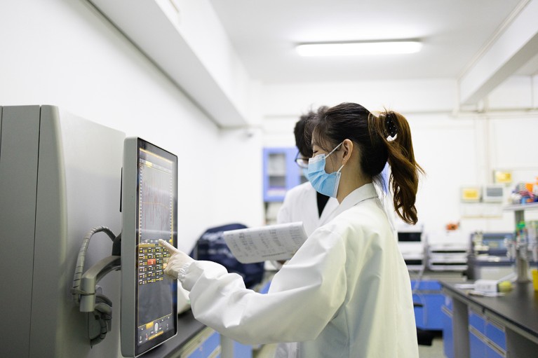 A young female Chinese researcher in a laboratory using a touch screen to programme a machine.