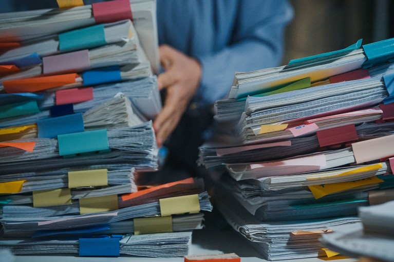 Close up view of a person searching through several large piles of bound paper documents.