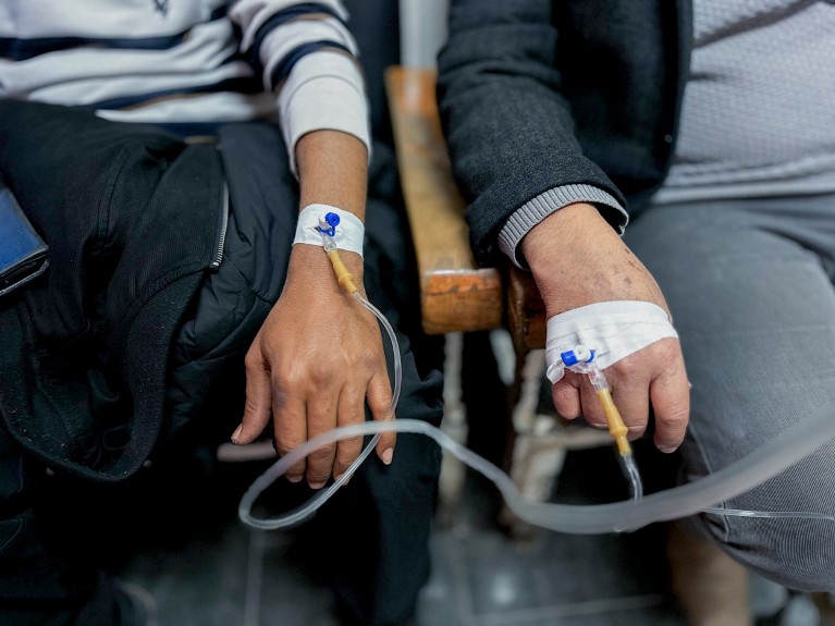 Close-up of two people with IV cannulas taped to their hands receiving treatment