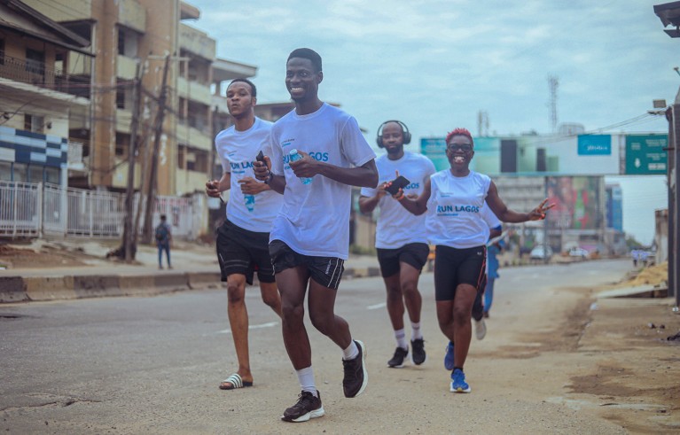 Tolullah Oni runs down a city road with a group of three other participants. They are all wearing matching white t-shirts.