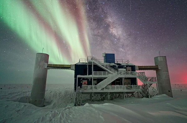 The IceCube Laboratory is seen under a starry night sky, with the Milky Way appearing in the background next to striking auroras.