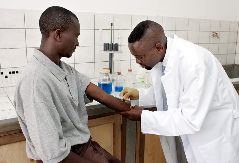 A male medical worker taking a blood sample from a seated man in a laboratory in the Democratic Republic of the Congo.