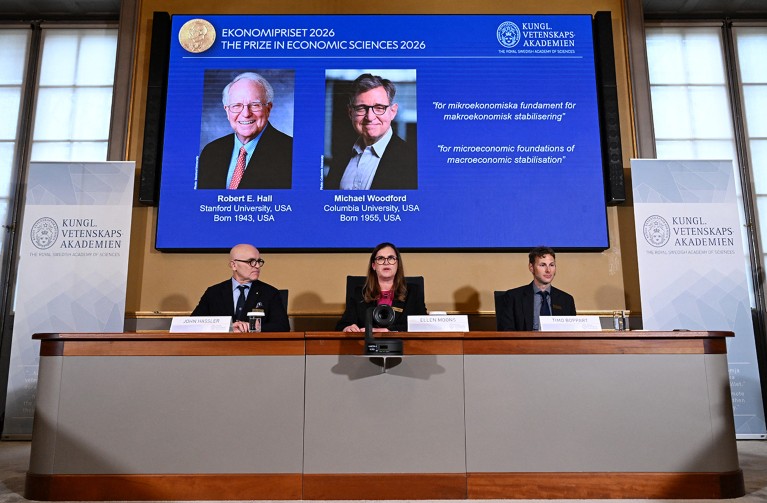 The three person panel at the Royal Academy of Sciences in Sweden, seated in front of a screen showing the joint winners of the 2026 Nobel prize in Economics.