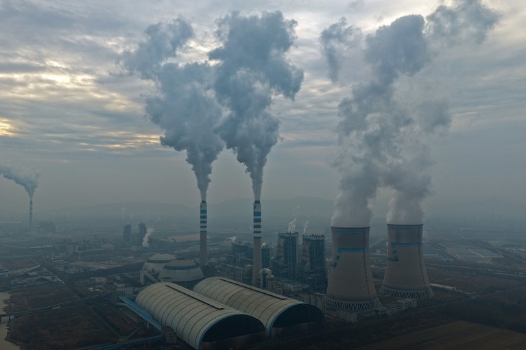 Aerial view showing power station chimney stacks, emitting smoke and water vapour into a grey sky.