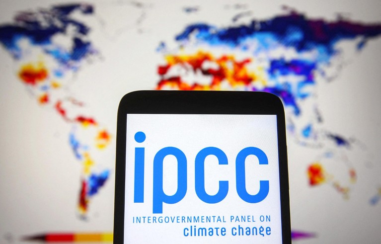 A smartphone displaying a blue IPCC logo, in front of a blurred world map in red, blue and yellow.