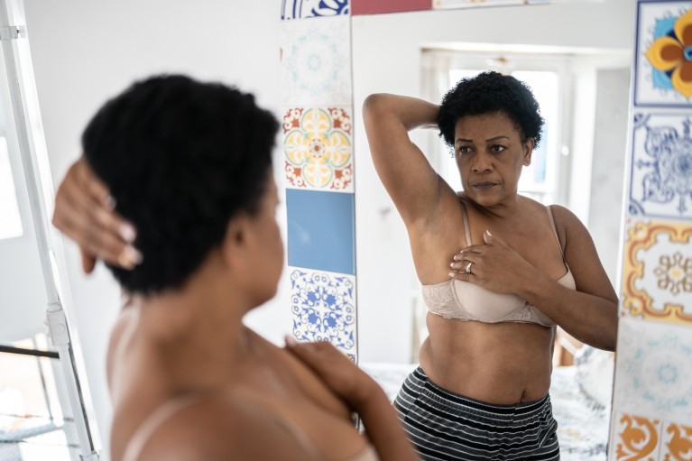 Middle-aged black woman standing in front of a mirror wearing a bra