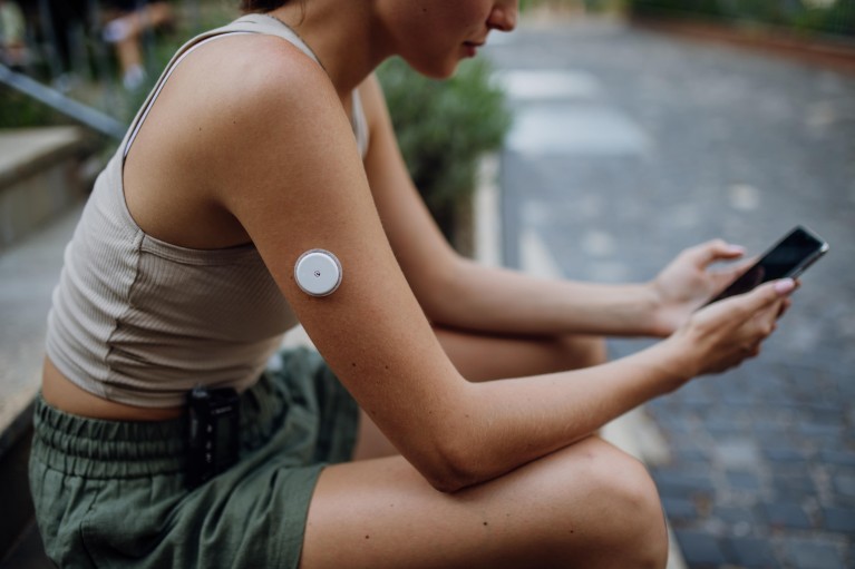 A woman holds a mobile phone towards a white plastic sensor attached to her upper arm