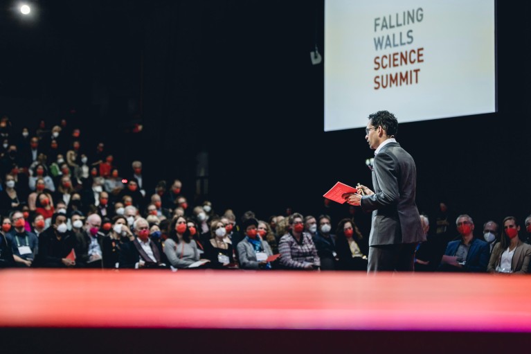 A presenter on stage at the Falling Walls Science Summit, speaking to an audience in the auditorium
