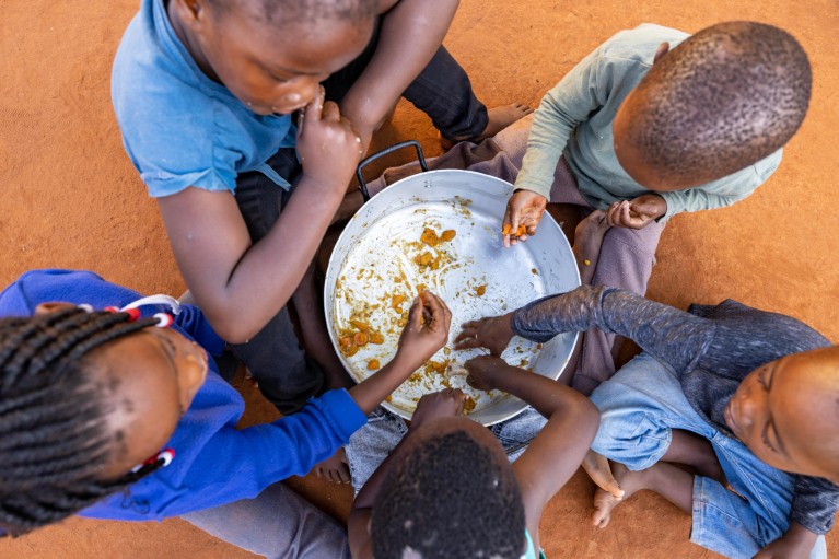 A group of five children sharing scraps of food from a bowl