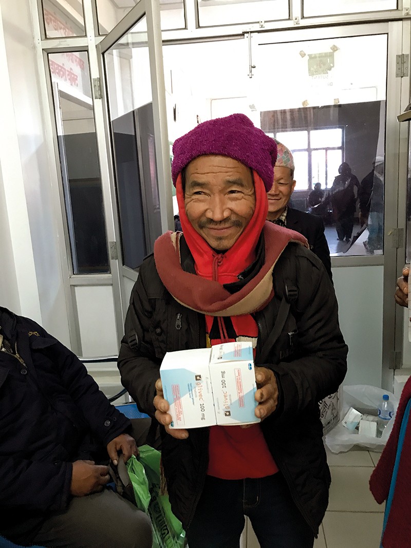 A smiling man holds up boxes containing cancer drugs.