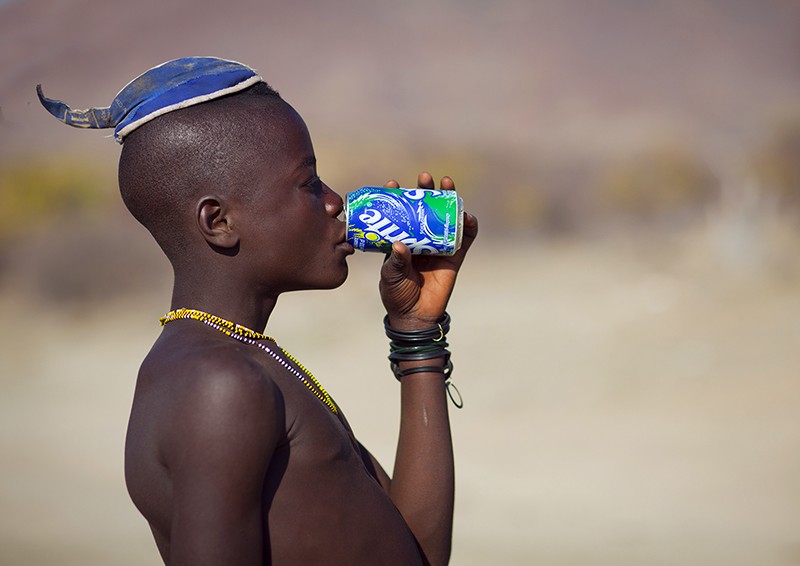 Muhimba young man with traditional hairstyle drinking a can of sprite in Iona, Angola