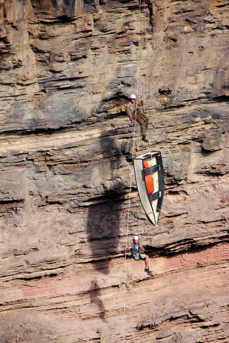 Two men and a boat hanging from rope on a cliff face
