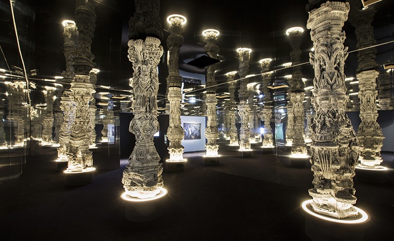 Intricate architectural columns, lit from above and below, in a dark room.